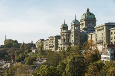 Das Bundeshaus in Bern an einem sonnigen Tag, umgeben von Herbstbäumen.