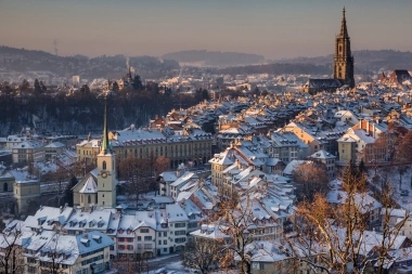 Un paesaggio urbano innevato con edifici storici e una grande chiesa sullo sfondo.