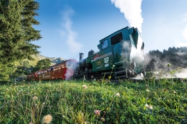 Eine dampfende grüne Lokomotive der Brienz Rothorn Bahn auf einer Bergstrecke.