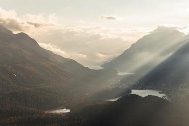 Landschaft mit Bergen im Morgenlicht, einem Tal und einem Gleitschirmflieger.