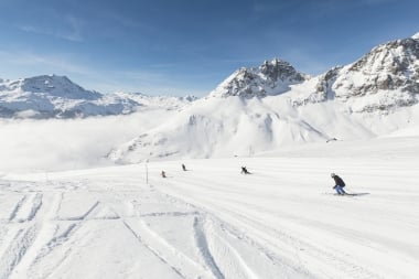 Skifahrer auf einer schneebedeckten Piste in den Bergen bei blauem Himmel.