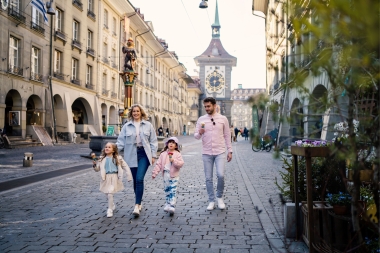 Eine Familie spaziert bei Sonnenschein durch die Altstadt von Bern und isst Eis.