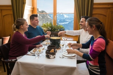 A group of four people enjoying fondue at a restaurant with a mountain view.