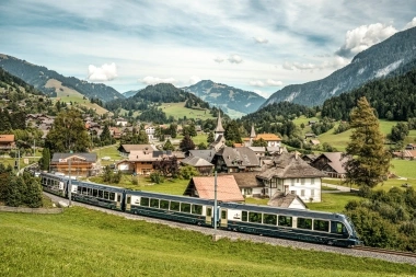 Eine idyllische Berglandschaft mit einem Zug, der durch ein malerisches Dorf fährt.