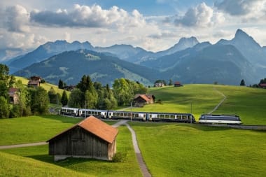 A train ride through a green hilly landscape with mountains in the background.