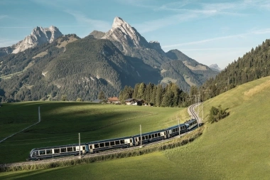 Train passes through green hills in front of a mountainous landscape.