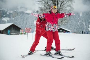 A ski instructor helps a student learn to ski in a snow-covered landscape.