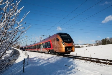 A red train is traveling on snow-covered tracks under a blue sky.