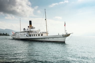 Ein weisses Dampfschiff fährt auf einem See unter bewölktem Himmel.