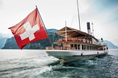 Una nave con bandiera svizzera naviga su un lago circondato da montagne.