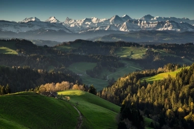 A vast mountain landscape with green hills and snow-capped peaks in the background.