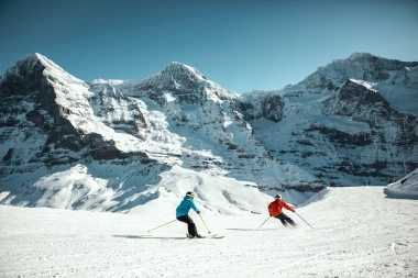 Zwei Skifahrer auf einer verschneiten Piste vor beeindruckender Bergkulisse.