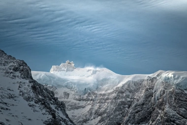 Eine verschneite Berglandschaft mit einem Gebäude auf dem Gipfel unter blauem Himmel.