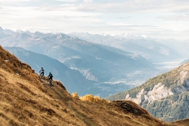 Two mountain bikers on a mountain trail with a wide valley view.
