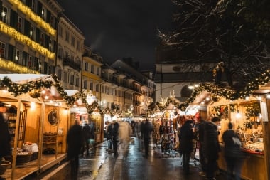 A festively lit Christmas market street with decorated stalls at night.