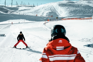 Une skieuse sur une piste damée, montagnes enneigées au loin.