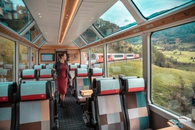 A woman walks through an empty panoramic train with large windows offering a view of the landscape.