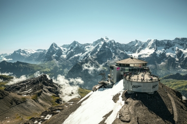 Eine Bergstation mit Aussichtsplattform auf einem verschneiten Gipfel vor einer Bergkette.