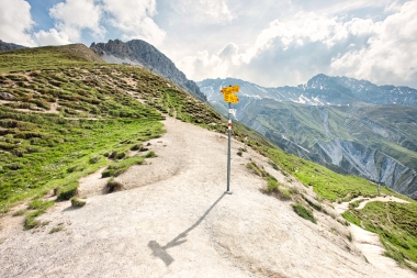 Un paesaggio montano con un sentiero escursionistico e un cartello nelle Alpi.