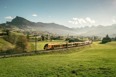 A train passing through green hills with mountains in the background.