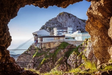 Un chalet de montagne moderne sur un sommet rocheux, vu à travers l'entrée d'une grotte.