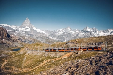 A red train travels through the mountain landscape in front of the Matterhorn.