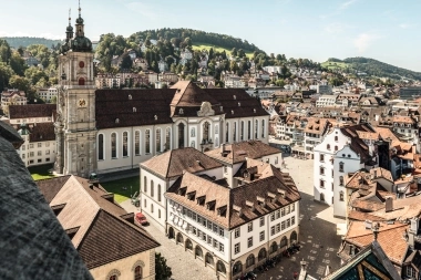 Aerial view of a historic church with surrounding buildings and hills in the background.