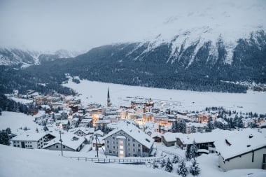 Eine verschneite Berglandschaft mit einem beleuchteten Dorf in der Abenddämmerung.
