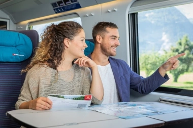 Una coppia è seduta su un treno, guarda fuori dal finestrino e tiene una mappa.