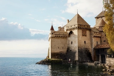 A medieval castle by a lake under a cloudy sky.