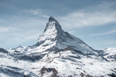 Eine verschneite Berglandschaft mit dem Matterhorn unter einem blauen Himmel.