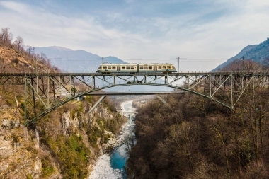 Train sur un pont au-dessus d'une gorge avec une rivière dans un paysage montagneux.