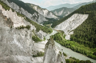 A picturesque river landscape in a gorge with densely wooded hills and a train on tracks.