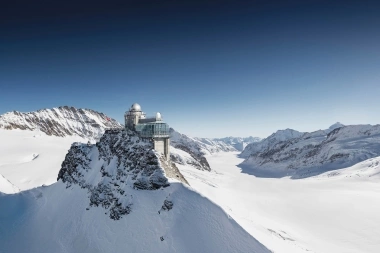 Una stazione di ricerca su una cima di montagna coperta di neve sotto un cielo blu.