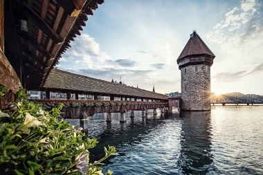 Eine alte Holzbrücke mit einem Turm im Wasser bei Sonnenuntergang.