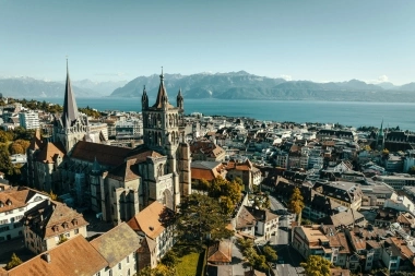 Vista aerea di una chiesa storica in una città con un lago e montagne sullo sfondo.