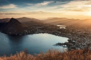 Sonnenuntergang über einer Stadt am See mit Bergen im Hintergrund.