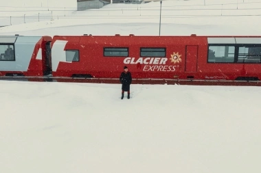 Une personne se tient dans la neige devant un train rouge "Glacier Express".