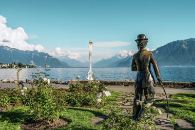 Eine Statue in einem Garten mit Blick auf einen See und Berge, in der Ferne eine grosse Gabel.