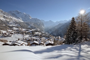 A snowy mountain landscape with a village in the valley and a sunny sky.