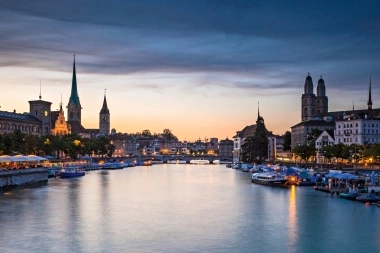 Coucher de soleil sur une ville avec une rivière, un pont et des bâtiments historiques.