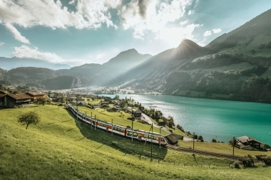 An idyllic mountain landscape with a train passing by a lake.
