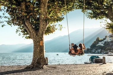 Two women sit on a swing and look out over the lake
