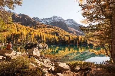 Eine Frau sitzt am idyllischen Bergsee umgeben von herbstlichen Bäumen
