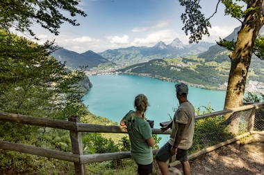 A hiking couple stands in Seelisberg near the Marienhöhe, looking out over the Rütli Meadow, Lake Uri, Brunnen, and the two Mythen peaks.