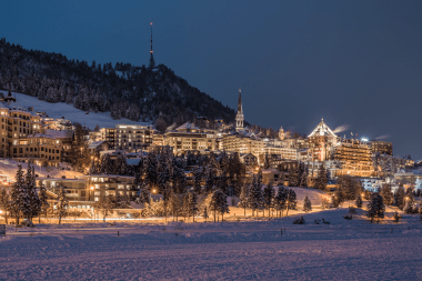 Eine winterliches Stadt bei Nacht, beleuchtete Gebäude und schneebedeckte Dächer.