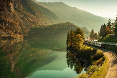 A train travels along a lake in autumnal surroundings