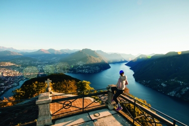 Una donna osserva un lago e un paesaggio montuoso da una terrazza su una montagna.