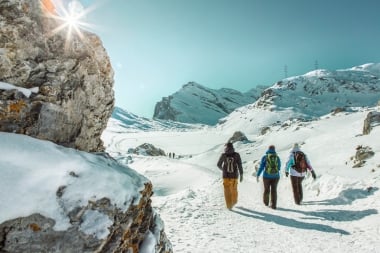 Drei Winterwanderer in einer verschneiten Berglandschaft unter blauem Himmel