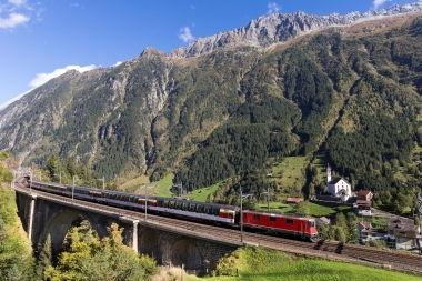 Una locomotiva rossa su un viadotto davanti a un paesaggio montano.